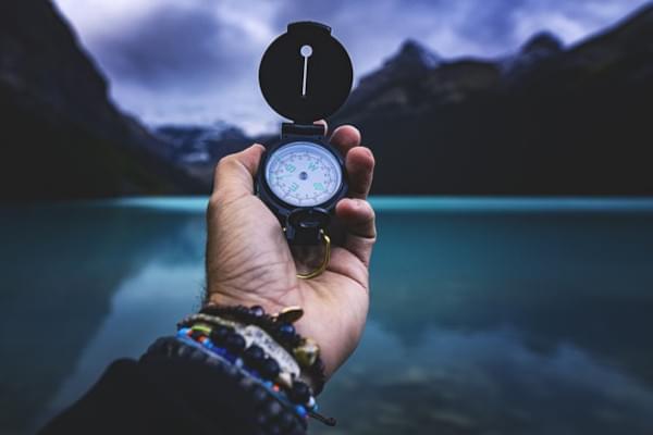 Homme tenant une boussole devant un lac entouré de montagnes